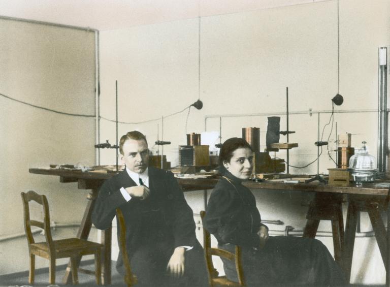 Farbfoto von Otto Hahn mit Les Meitner um 1910 in einem Labor sitzend.